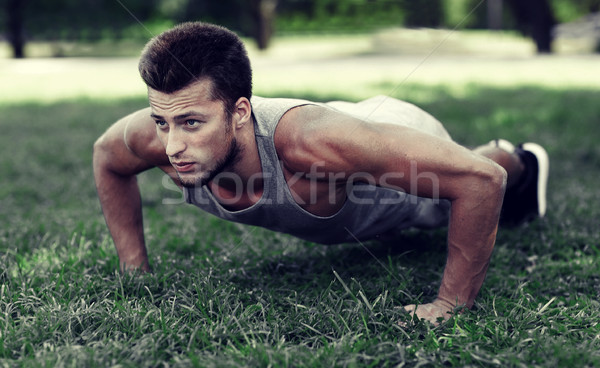 young man doing push ups on grass in summer park Stock photo © dolgachov