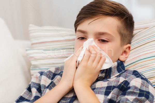 ill boy lying in bed and blowing his nose at home Stock photo © dolgachov