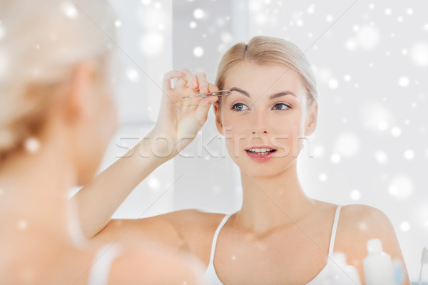 woman with tweezers tweezing eyebrow at bathroom Stock photo © dolgachov