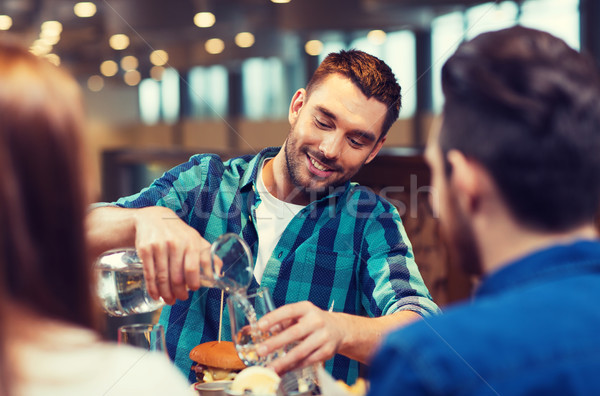 happy man with friends pouring water at restaurant Stock photo © dolgachov