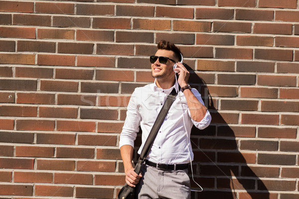 young man in headphones with bag over brickwall Stock photo © dolgachov