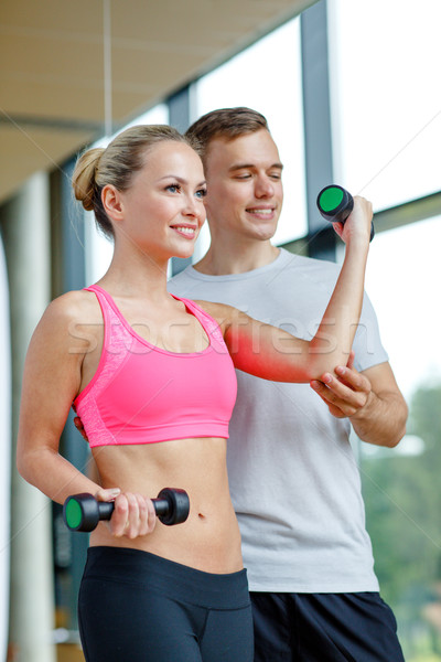 Stock photo: smiling young woman with personal trainer in gym