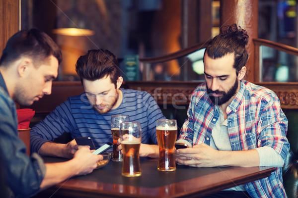 male friends with smartphones drinking beer at bar Stock photo © dolgachov