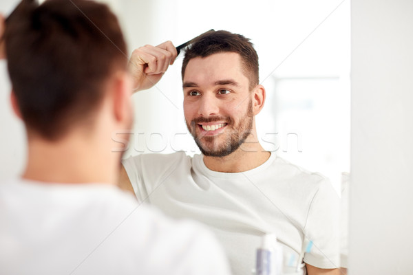 happy man brushing hair  with comb at bathroom Stock photo © dolgachov