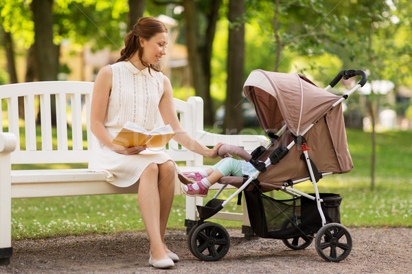 Stock photo: mother with child in stroller reading book at park