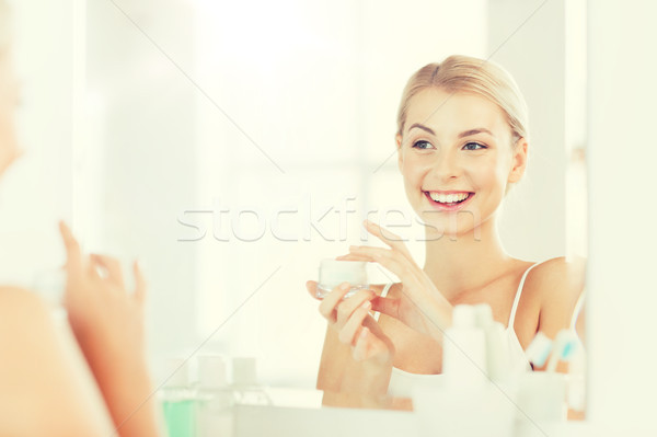 happy woman applying cream to face at bathroom Stock photo © dolgachov