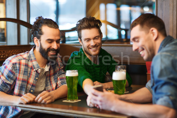 friends with smartphone drinking green beer at pub Stock photo © dolgachov