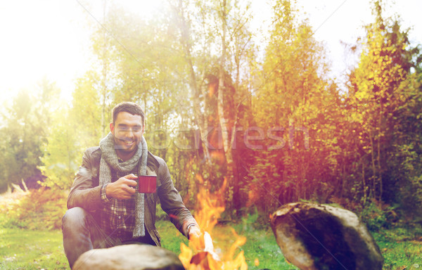 happy man drinking hot tea near camp fire Stock photo © dolgachov