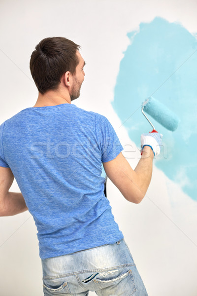 man with roller painting wall in blue at home Stock photo © dolgachov
