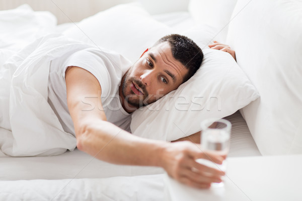 man in bed and reaching to glass of water at home Stock photo © dolgachov