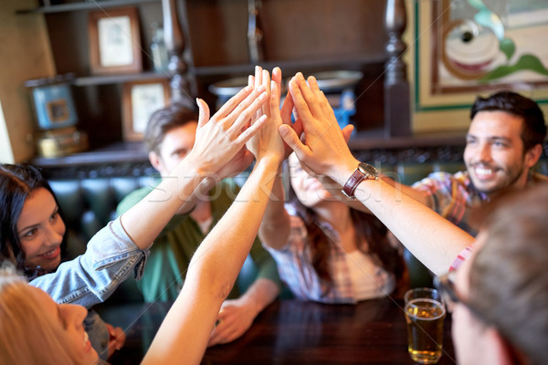 friends drinking beer and making high five at bar Stock photo © dolgachov