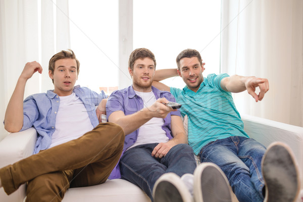 Stock photo: smiling friends with remote control at home
