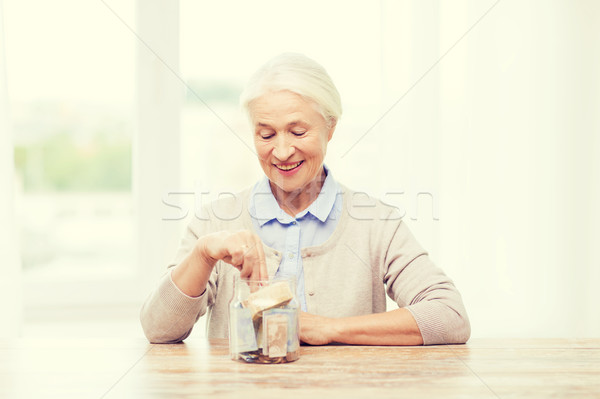 senior woman putting money into glass jar at home Stock photo © dolgachov