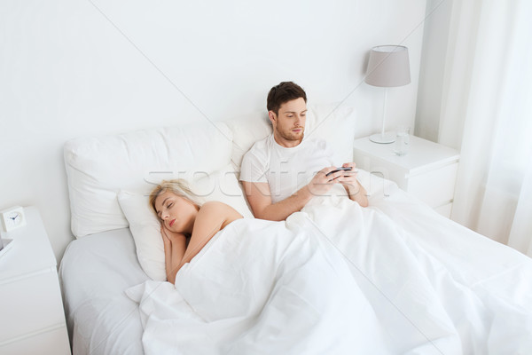 man texting message while woman is sleeping in bed Stock photo © dolgachov
