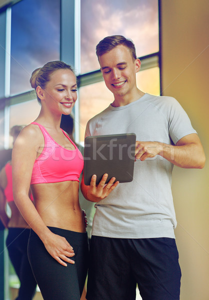 Stock photo: smiling young woman with personal trainer in gym