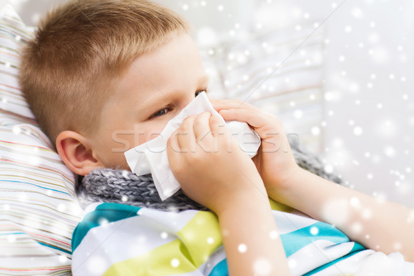 ill boy blowing nose with tissue at home Stock photo © dolgachov