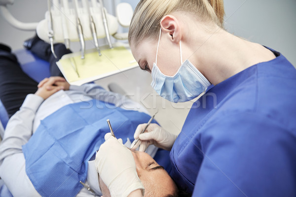 female dentist in mask checking male patient teeth Stock photo © dolgachov