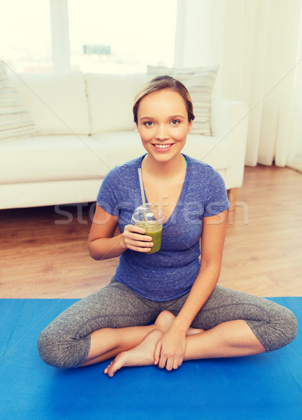 happy woman with smoothie sitting on mat at home Stock photo © dolgachov