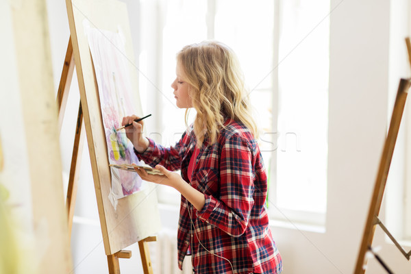 woman artist with easel painting at art studio Stock Photo by dolgachov