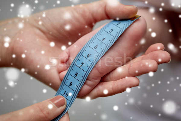 Stock photo: close up of hands with tape measuring baby foot