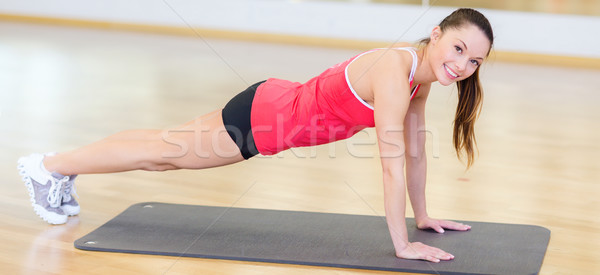 Stock photo: smiling woman doing plank on mat in gym