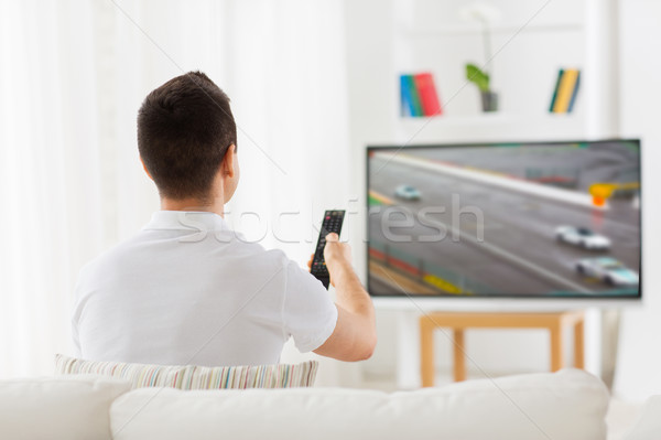 Stock photo: man with remote watching motorsports on tv at home