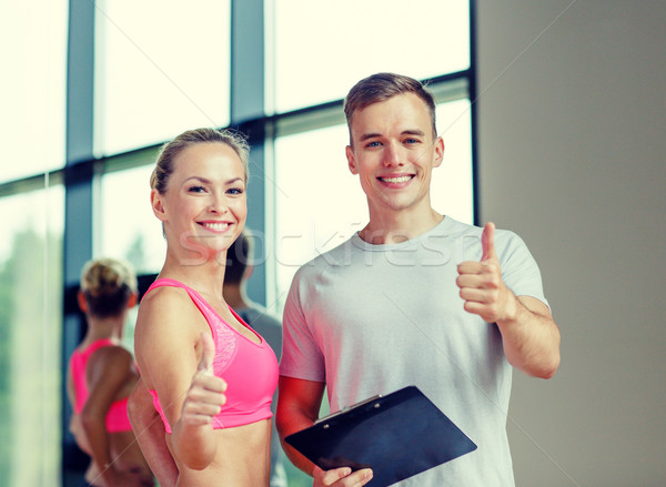 smiling young woman with personal trainer in gym Stock photo © dolgachov