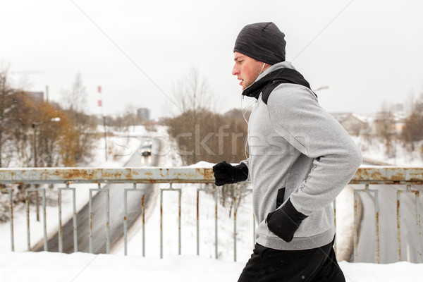 man in earphones running along winter bridge Stock photo © dolgachov