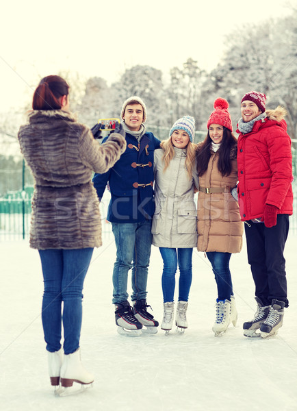 Stock photo: happy friends with smartphone on ice skating rink