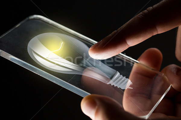 Stock photo: close up of hands with lightbulb smartphone