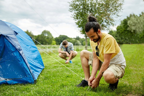 smiling friends setting up tent outdoors Stock photo © dolgachov