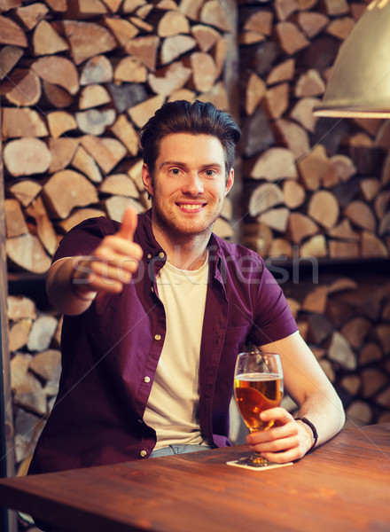happy man with beer showing thumbs up at bar Stock photo © dolgachov
