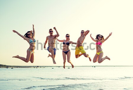 smiling friends dancing and jumping on beach Stock photo © dolgachov