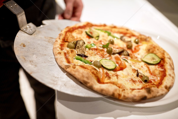 chef placing pizza from peel to plate at pizzeria Stock photo © dolgachov