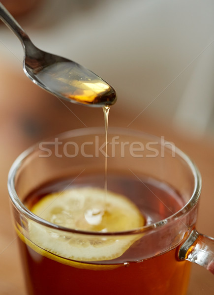 Stock photo: close up of woman adding honey to tea with lemon