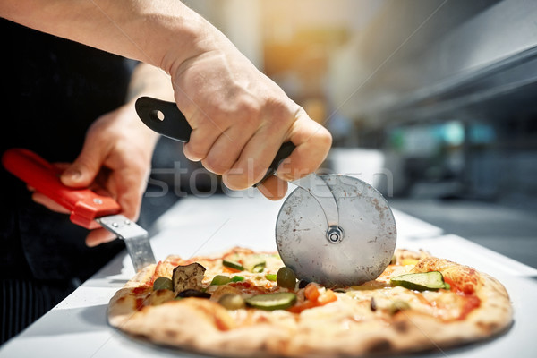cook cutting pizza to pieces at pizzeria Stock photo © dolgachov