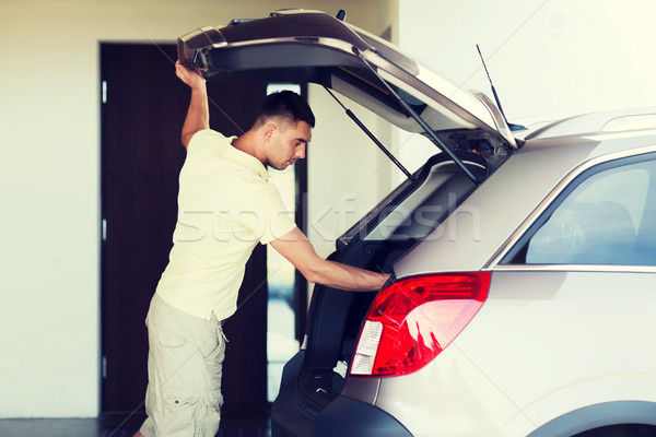 young man with open car trunk at parking space Stock photo © dolgachov