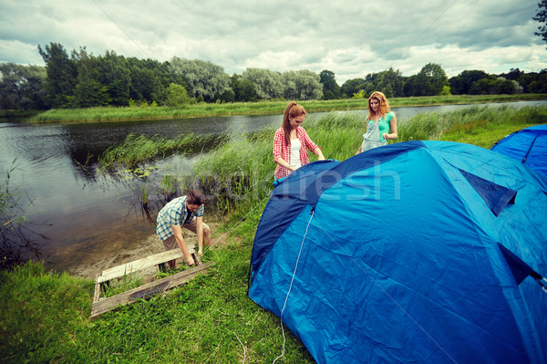 group of smiling friends setting up tent outdoors Stock photo © dolgachov