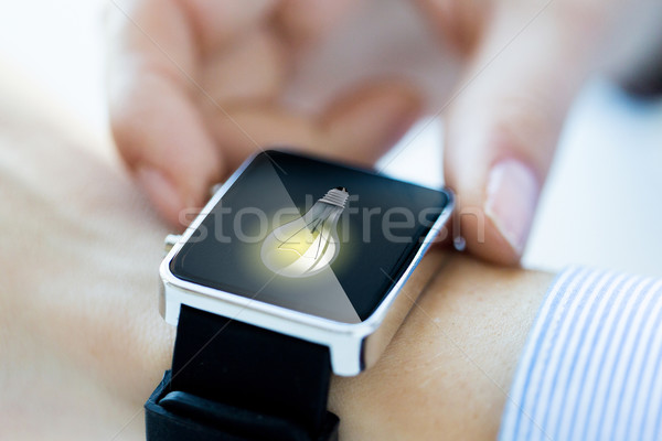 Stock photo: close up of hands with lightbulb on smartwatch