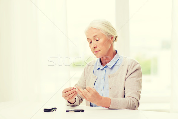 senior woman with glucometer checking blood sugar Stock photo © dolgachov
