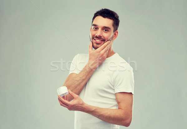 happy young man applying cream to face over gray Stock photo © dolgachov