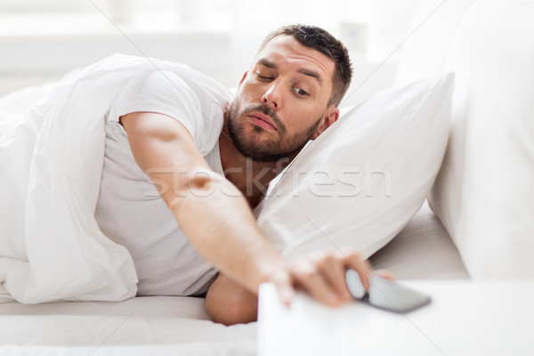 young man reaching for smartphone in bed Stock photo © dolgachov