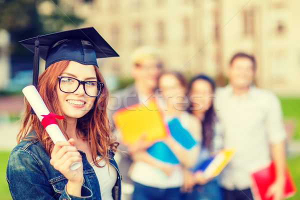 smiling teenage girl in corner-cap with diploma Stock photo © dolgachov