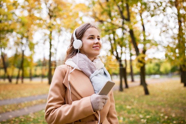woman with smartphone and earphones in autumn park Stock photo © dolgachov