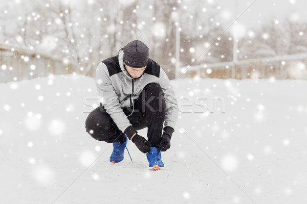 man with earphones tying sports shoe in winter Stock photo © dolgachov
