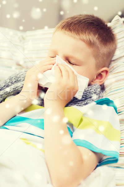 ill boy blowing nose with tissue at home Stock photo © dolgachov