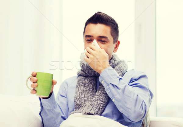 Stock photo: ill man with flu drinking tea and blowing nose