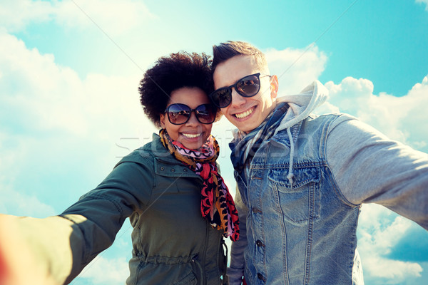 Stock photo: happy teenage couple taking selfie over blue sky