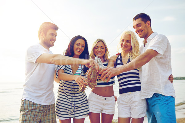 Stock photo: smiling friends clinking bottles on beach