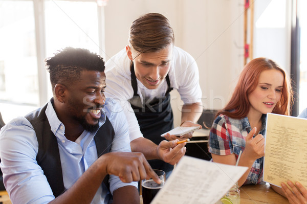 Stock photo: waiter and friends with menu and drinks at bar